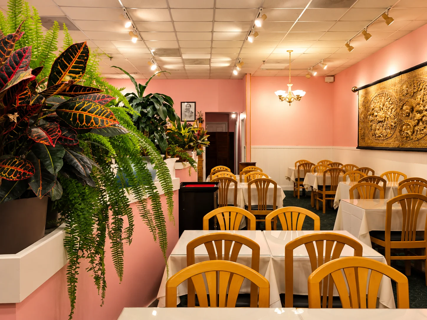 Restaurant dining room with tropical plants, white tablecloths, and warm lighting