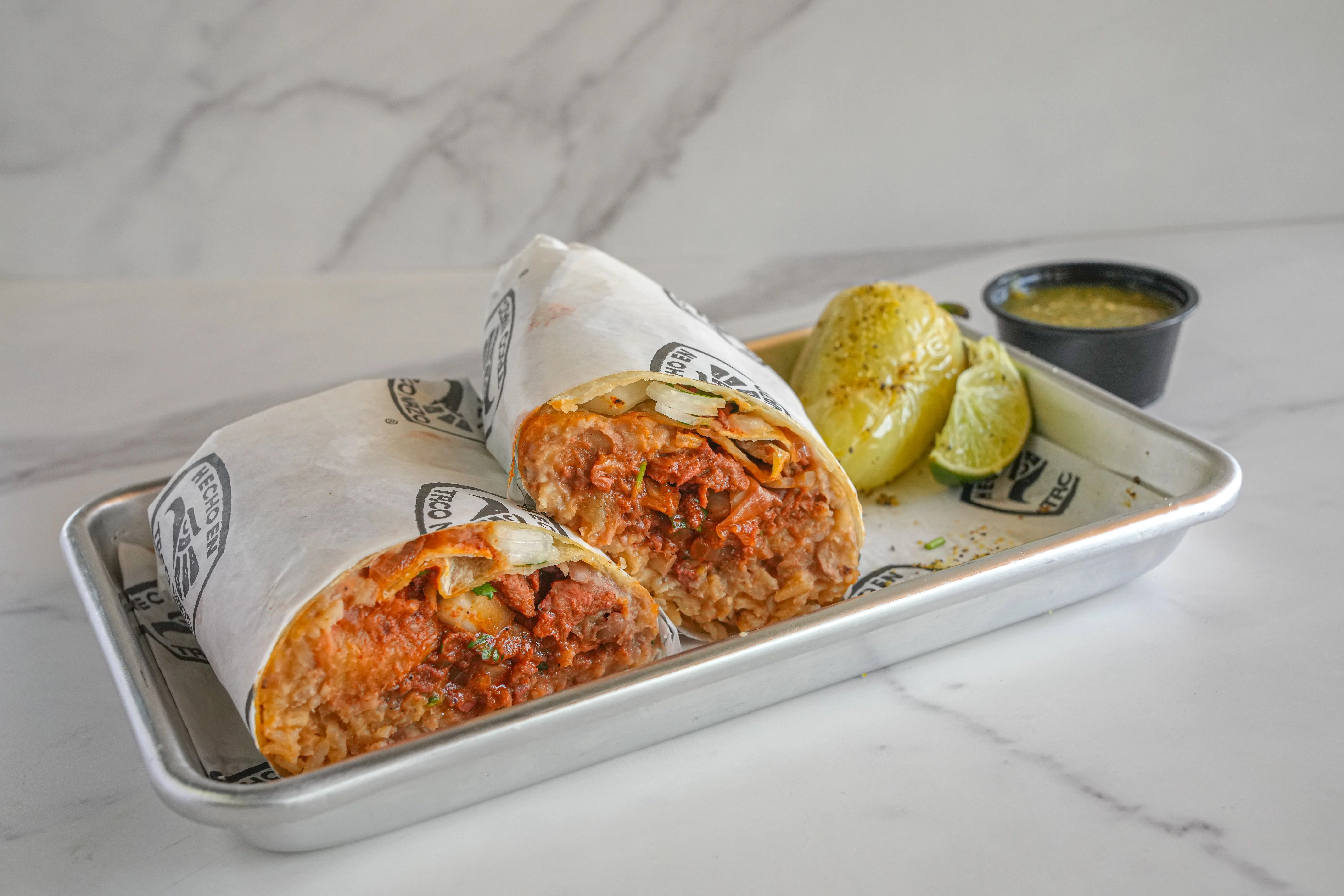 Plated Al Pastor burrito with chile, lime, and salsa.