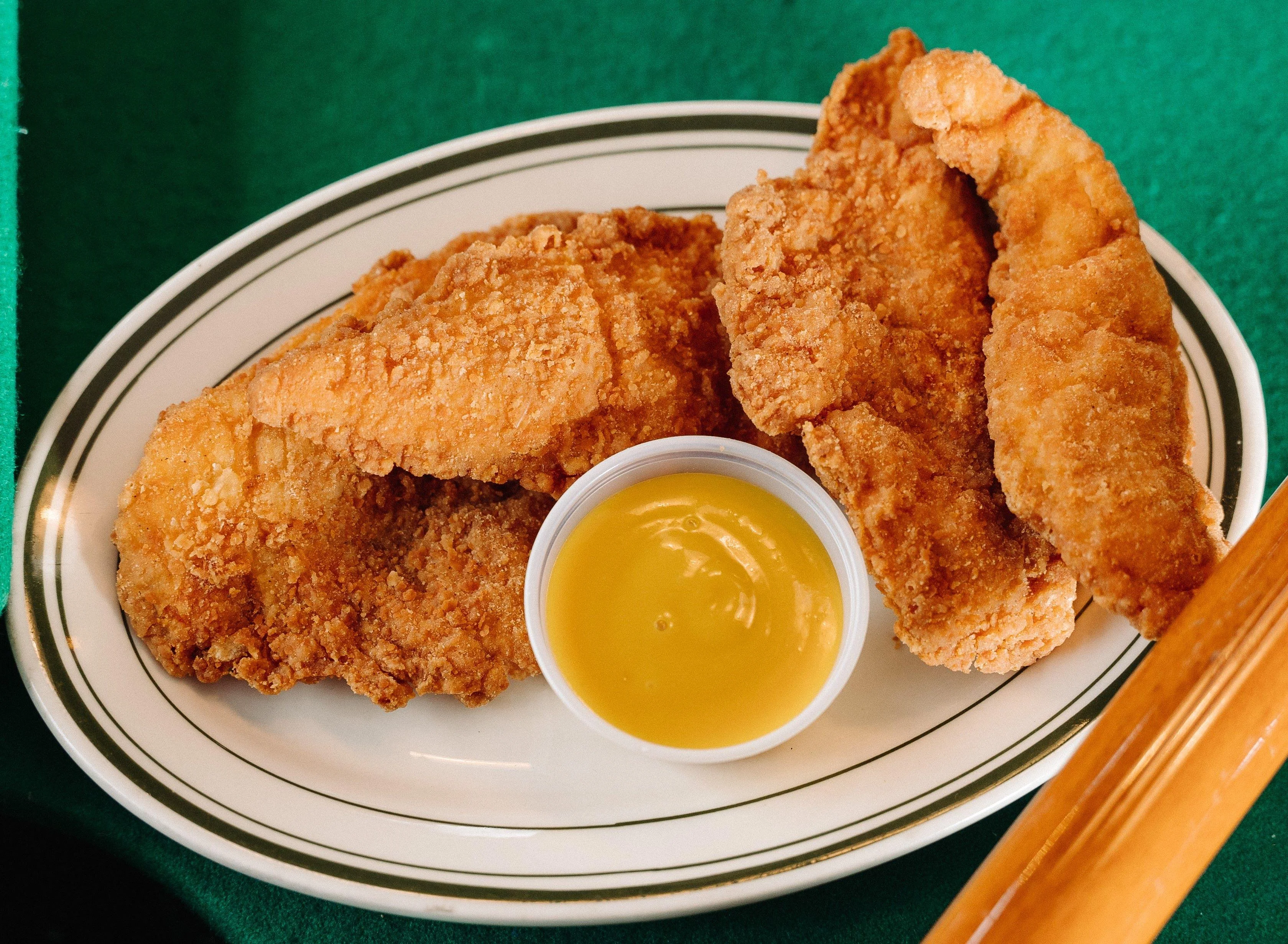 Three pieces of fried fish on a plate, accompanied by a small cup of yellow dipping sauce.