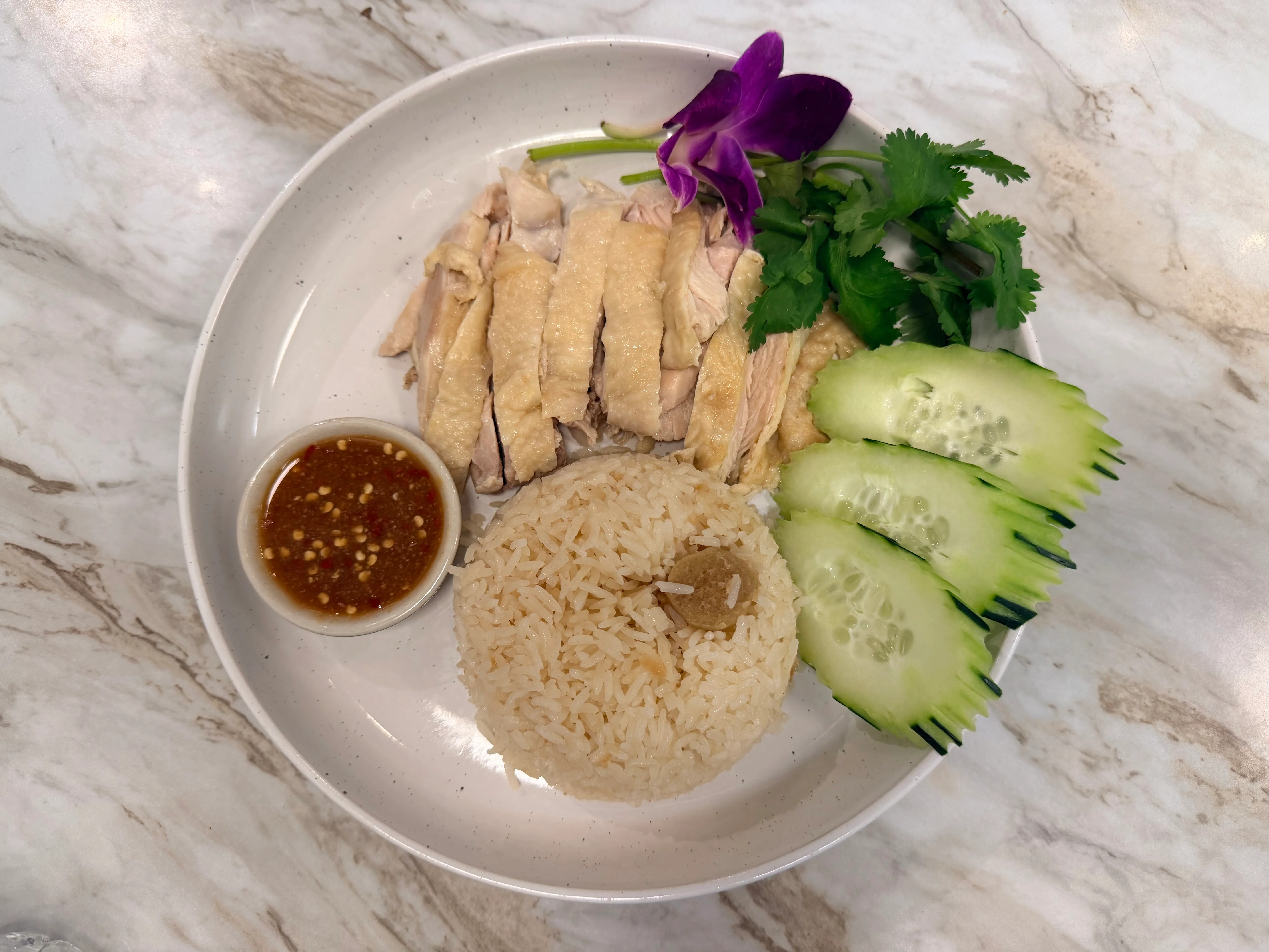 Hainanese chicken rice served with dipping sauce and cucumber slices