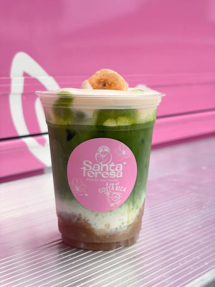 A colorful layered drink containing matcha, with a topping of whipped cream and a small cookie on top.