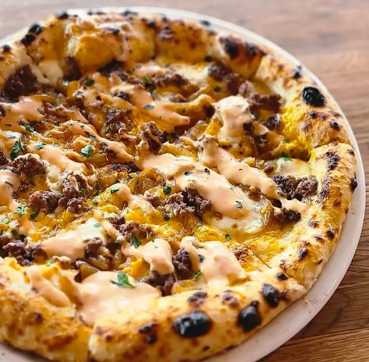 A pizza topped with ground meat, cheeses, and a drizzle of sauce, featuring a golden-brown crust.