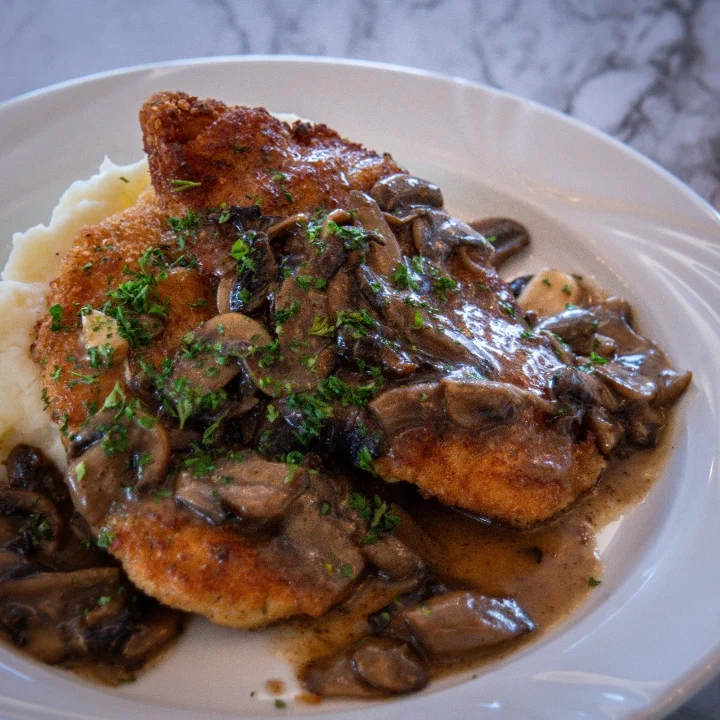 A plated dish of crispy chicken with a creamy mushroom sauce served alongside mashed potatoes.