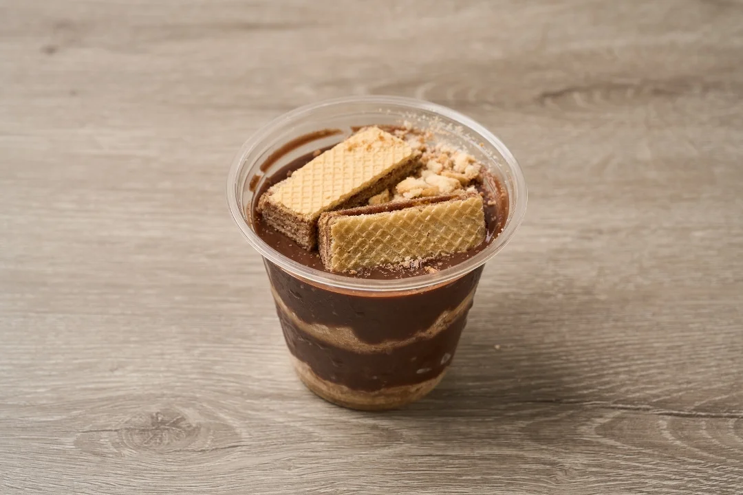 A cup of chocolate pudding layered with crushed cookies and topped with wafer biscuits. The rich brown color contrasts with the lighter layers below.