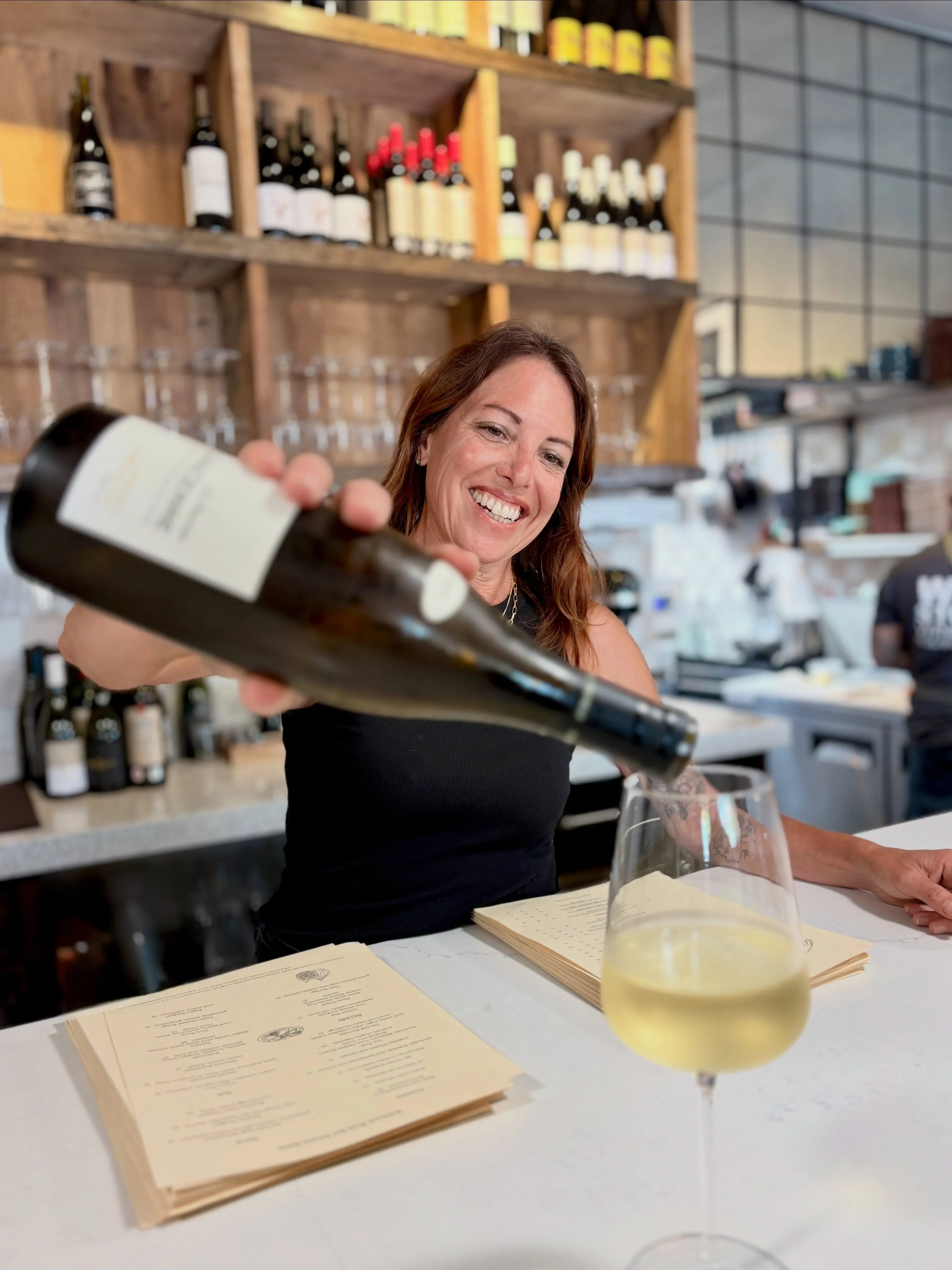 Person holding a bottle of wine and a glass in natural light