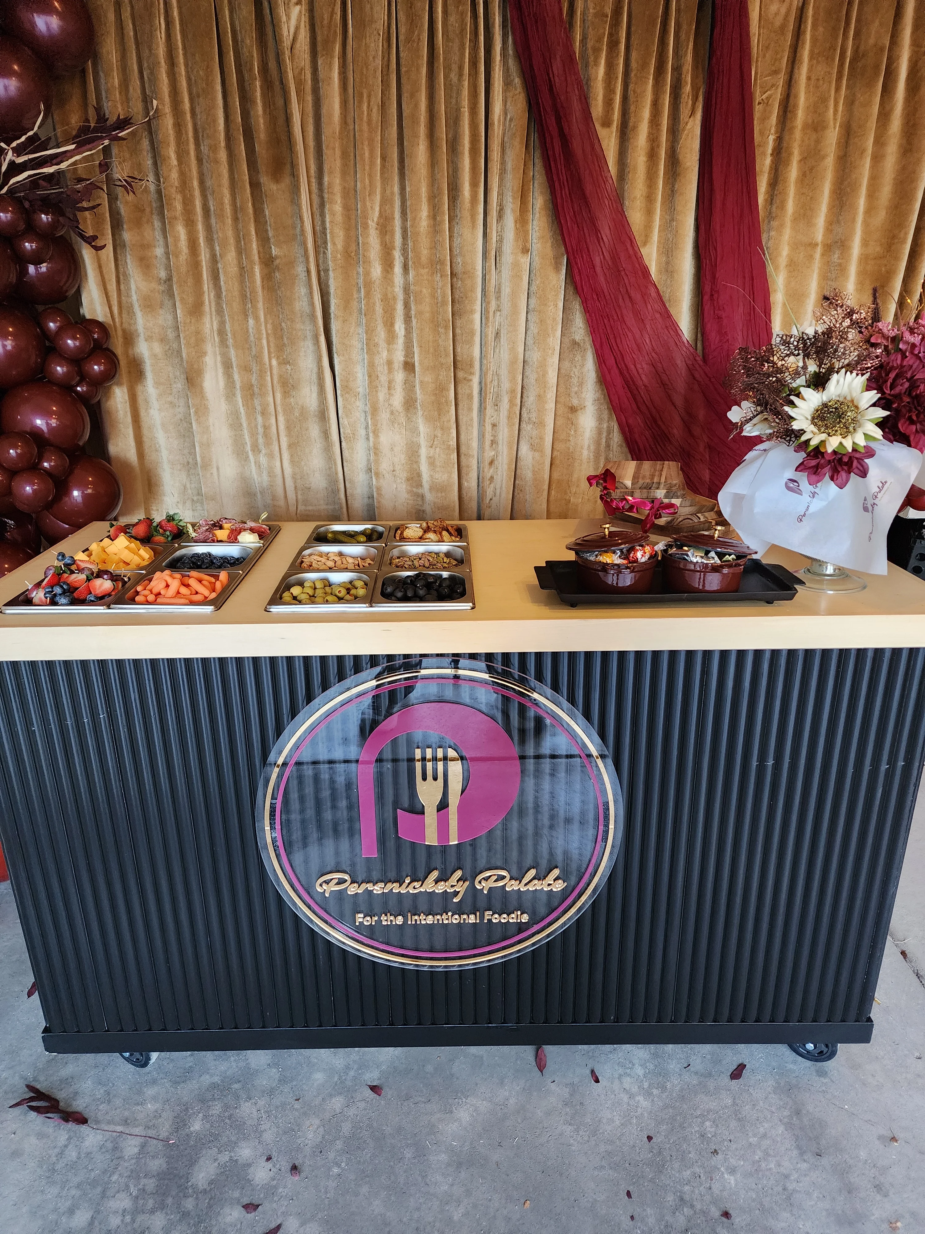 A beautifully arranged food display featuring a variety of fruits, cheeses, and snacks, set against an elegant backdrop.