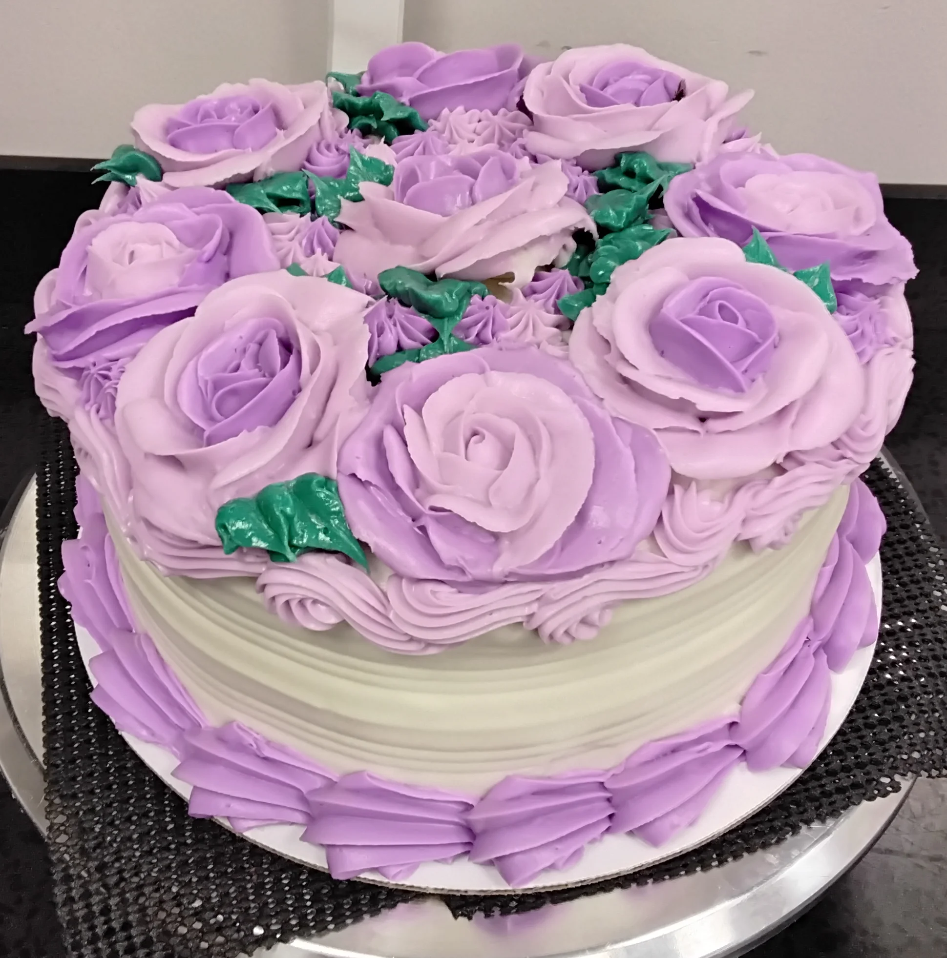 Round cake with an ombre of purple roses covering the top and a few green leaves sprinkled in.
