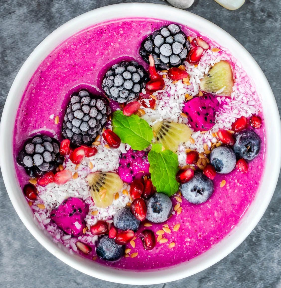 A colorful pink smoothie bowl adorned with blackberries, pomegranate seeds, and coconut flakes, along with dragon fruit accents.