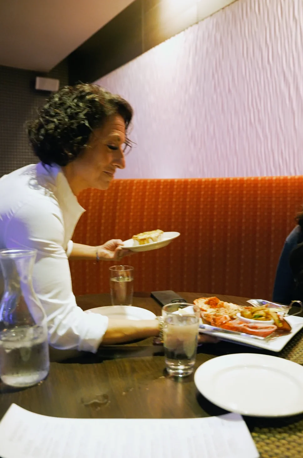 A woman serving food at a restaurant table with drinks and dishes.