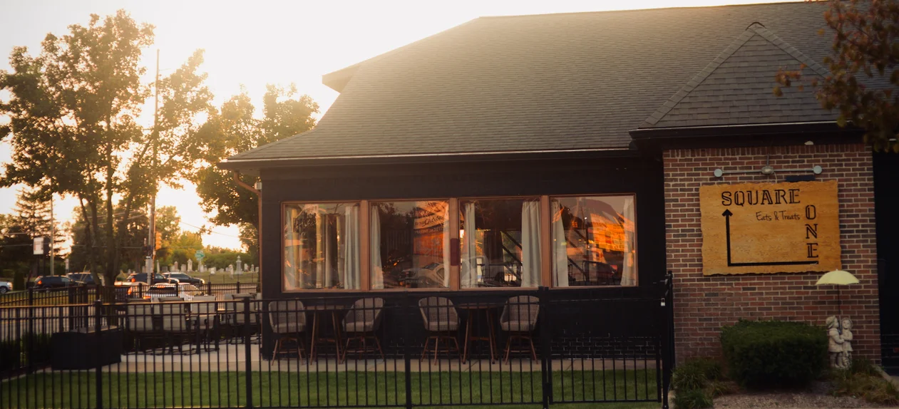 A stylish restaurant exterior with a black facade and large windows, surrounded by trees and outdoor seating.