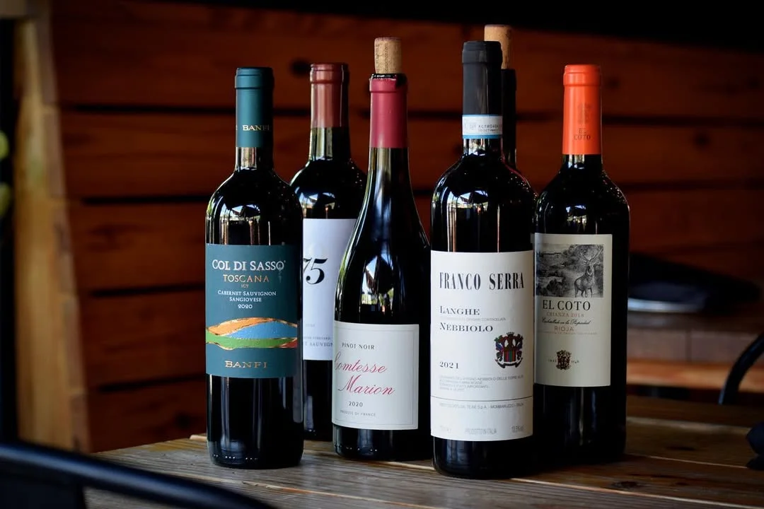 A collection of wine bottles featuring various labels and colors, arranged on a wooden table.