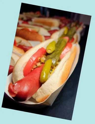Two women holding a tray of hot dogs with toppings, smiling together.