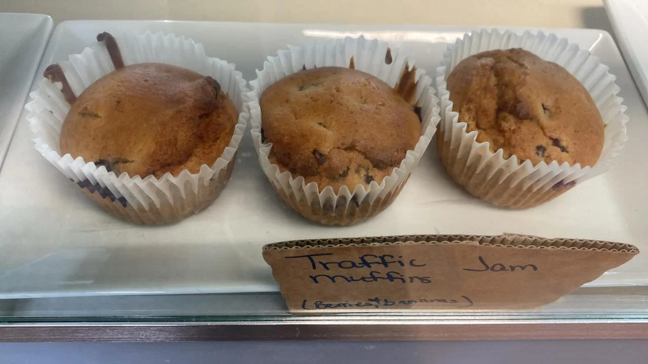 Three traffic jam muffins displayed in a bakery case, with a label indicating their flavor.