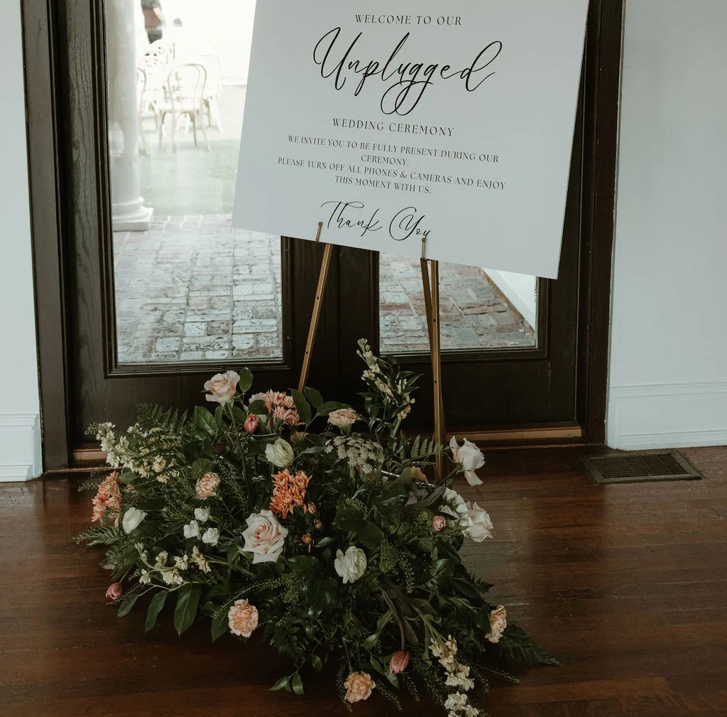 Welcome sign for an unplugged wedding ceremony with floral arrangement