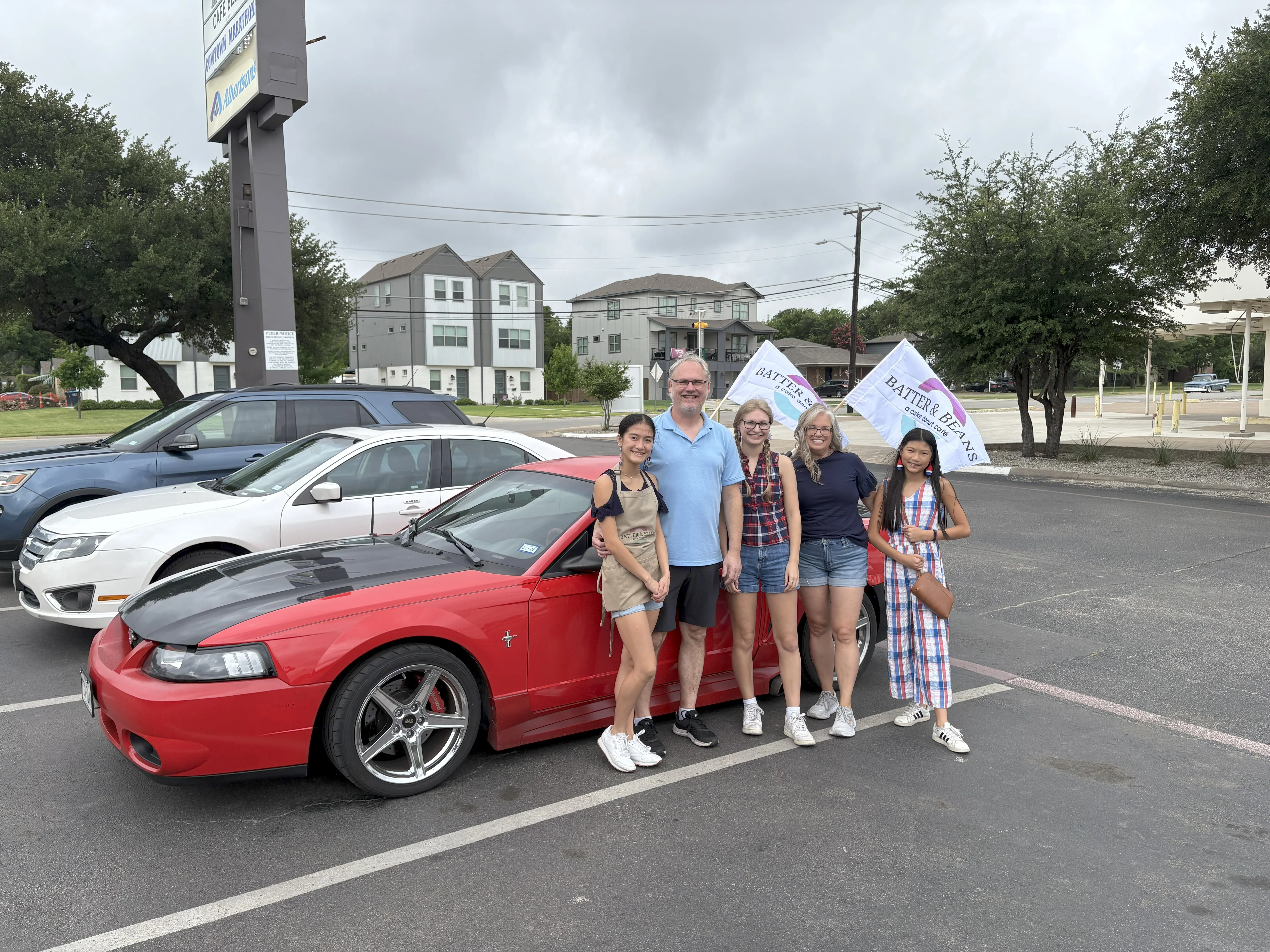 Group of friends posing with a red sports car and promotional flags