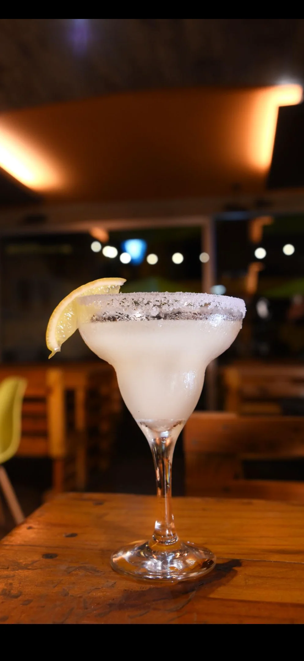 A refreshing margarita cocktail with a lemon slice on a wooden table.