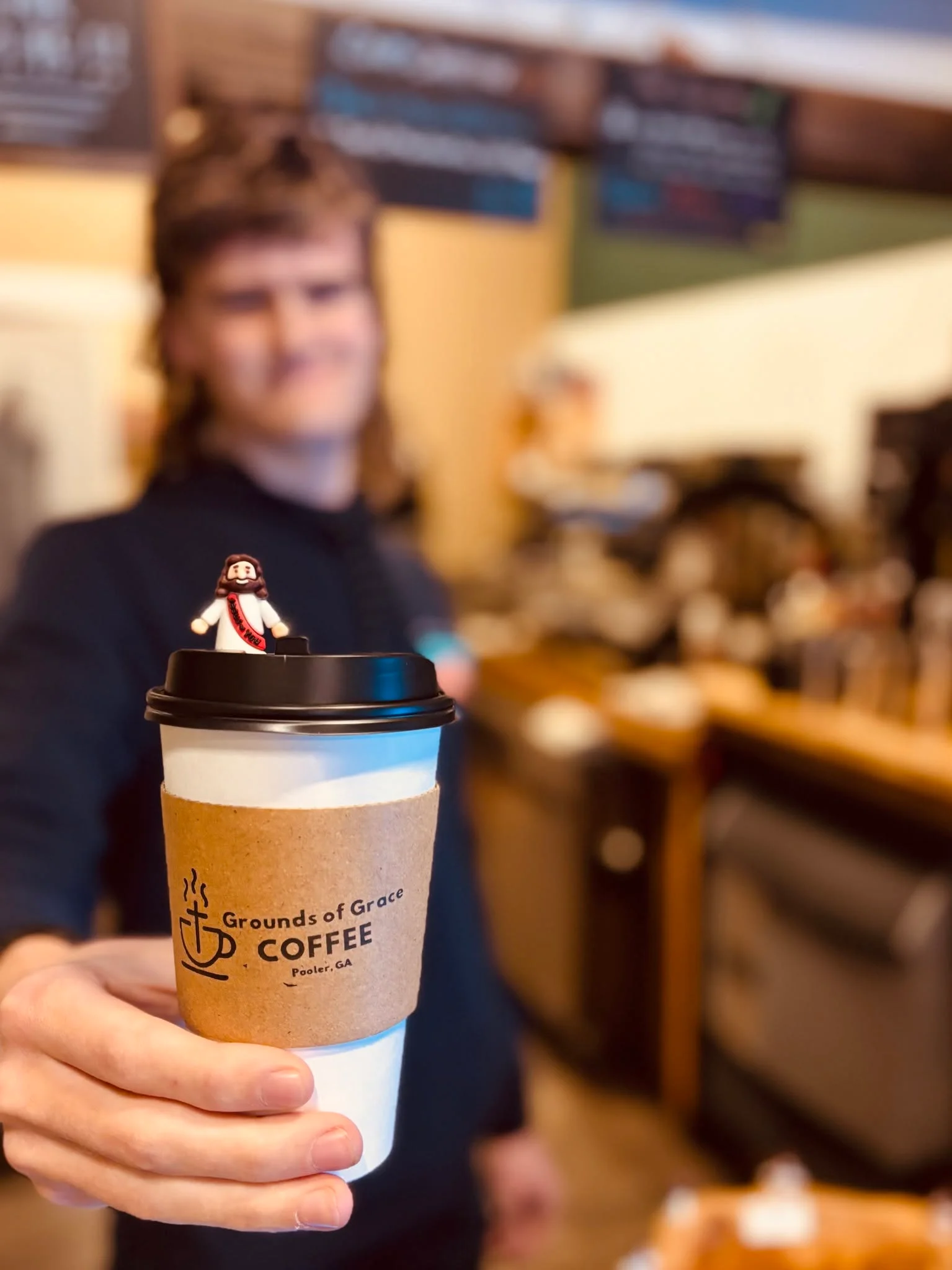 Barista holding a coffee cup with a playful figurine on top