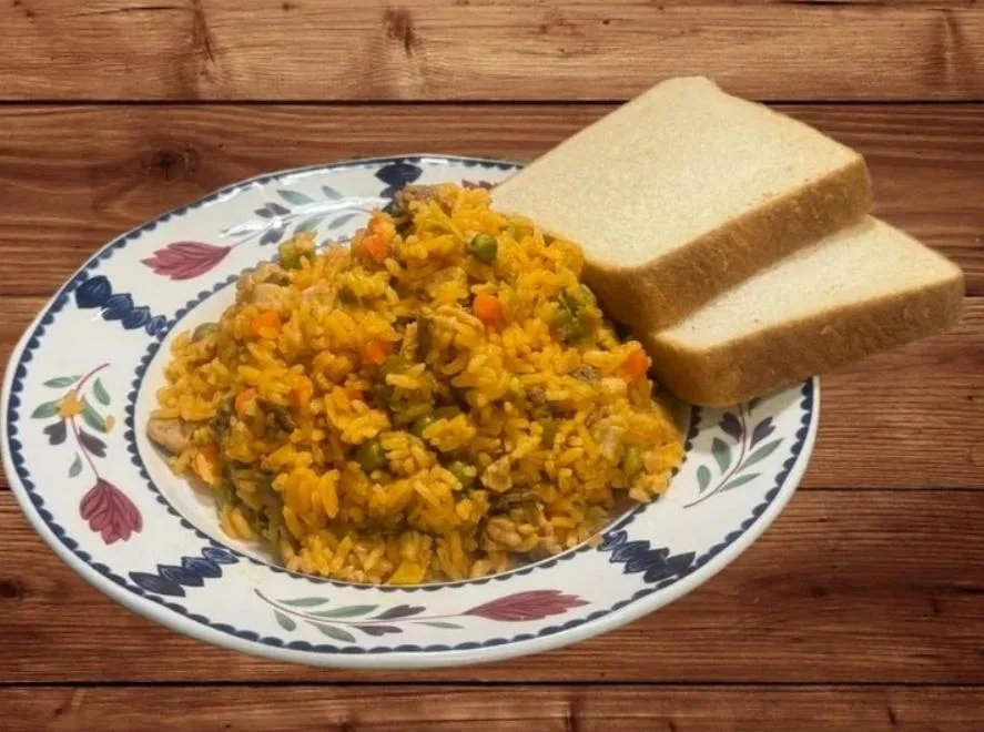 A serving of vibrant yellow rice mixed with vegetables, accompanied by two slices of bread on the side, arranged on a decorative plate.