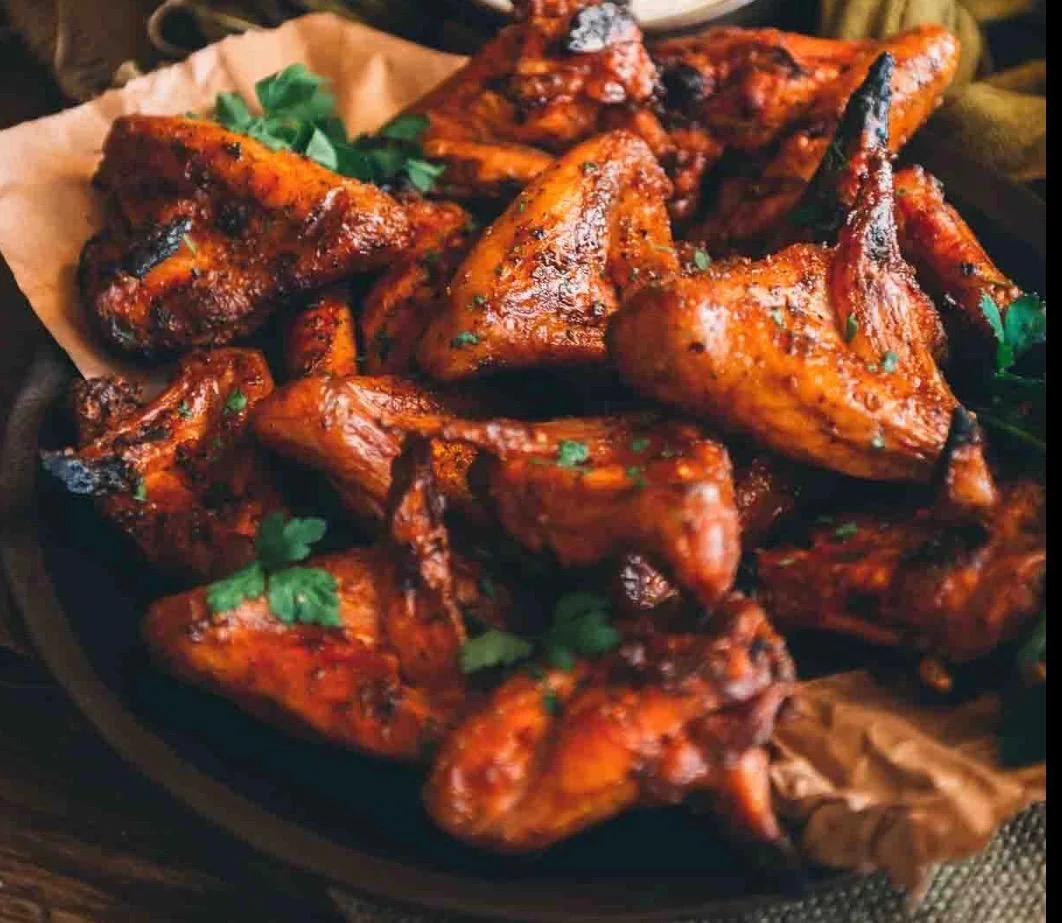 A close-up of a platter filled with beautifully cooked, spiced chicken wings garnished with fresh herbs.