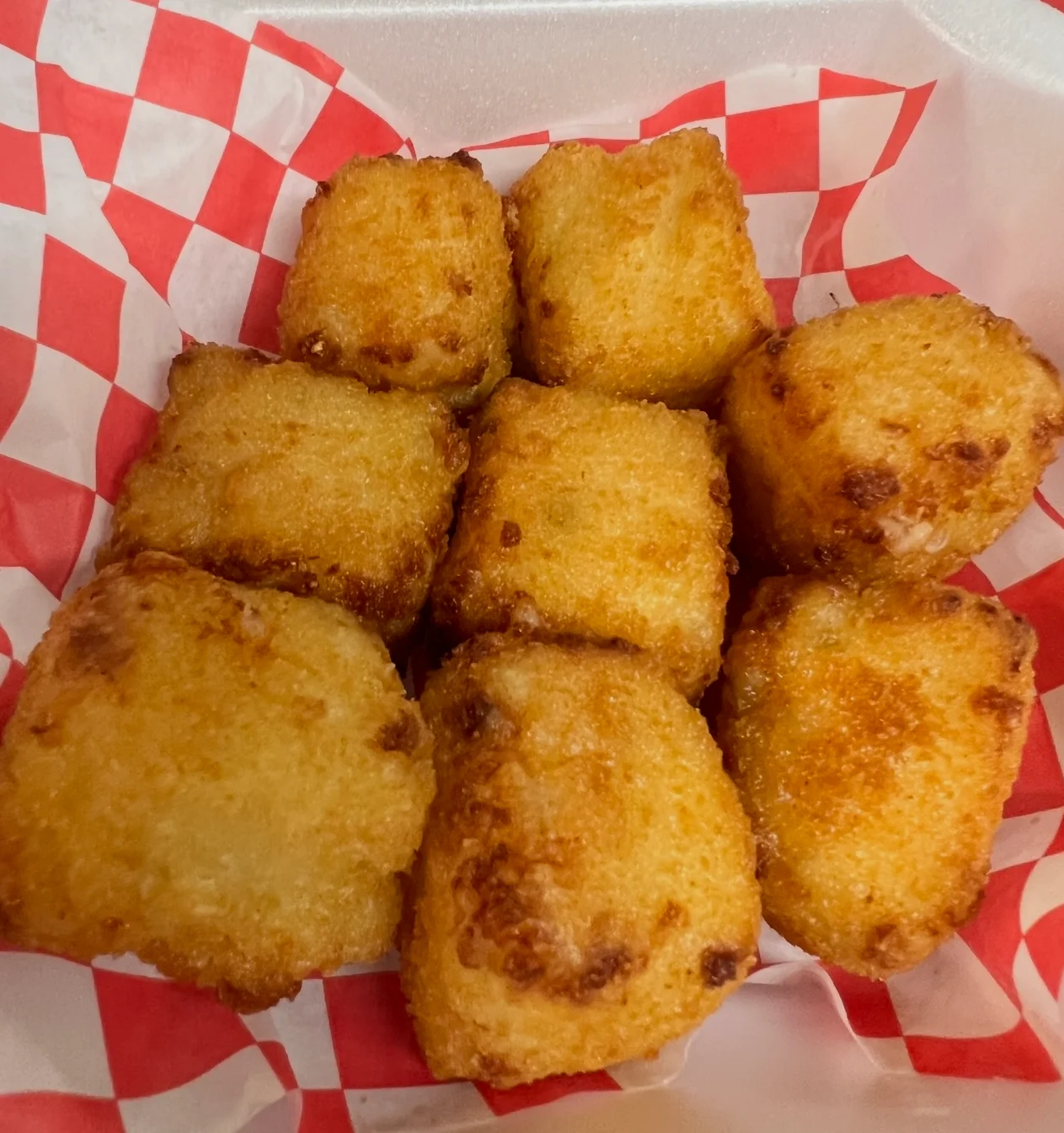 A serving of golden-brown fried bites arranged in a container, with a red and white checkered lining.