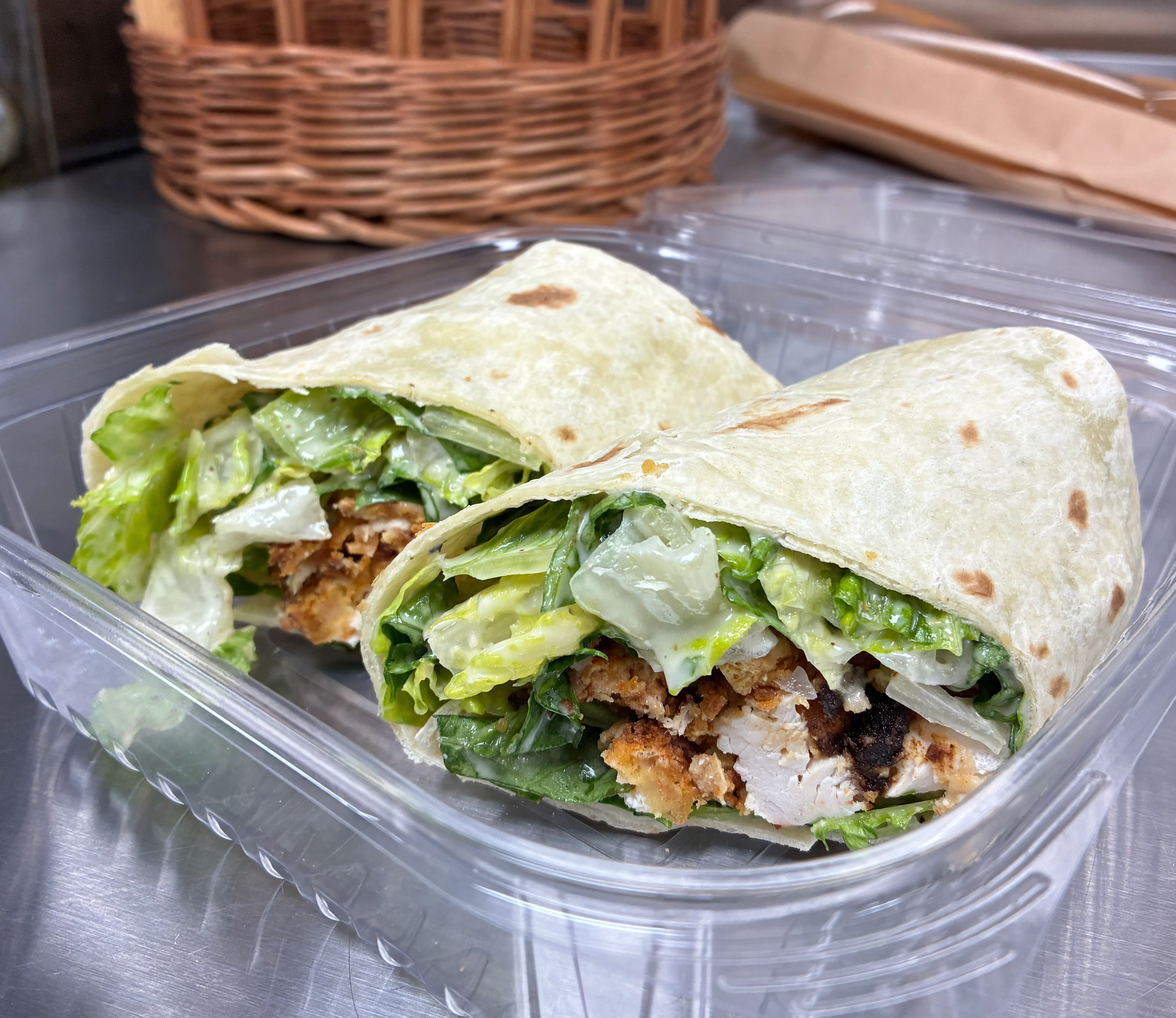 Two wraps filled with lettuce and grilled chicken in a clear container.