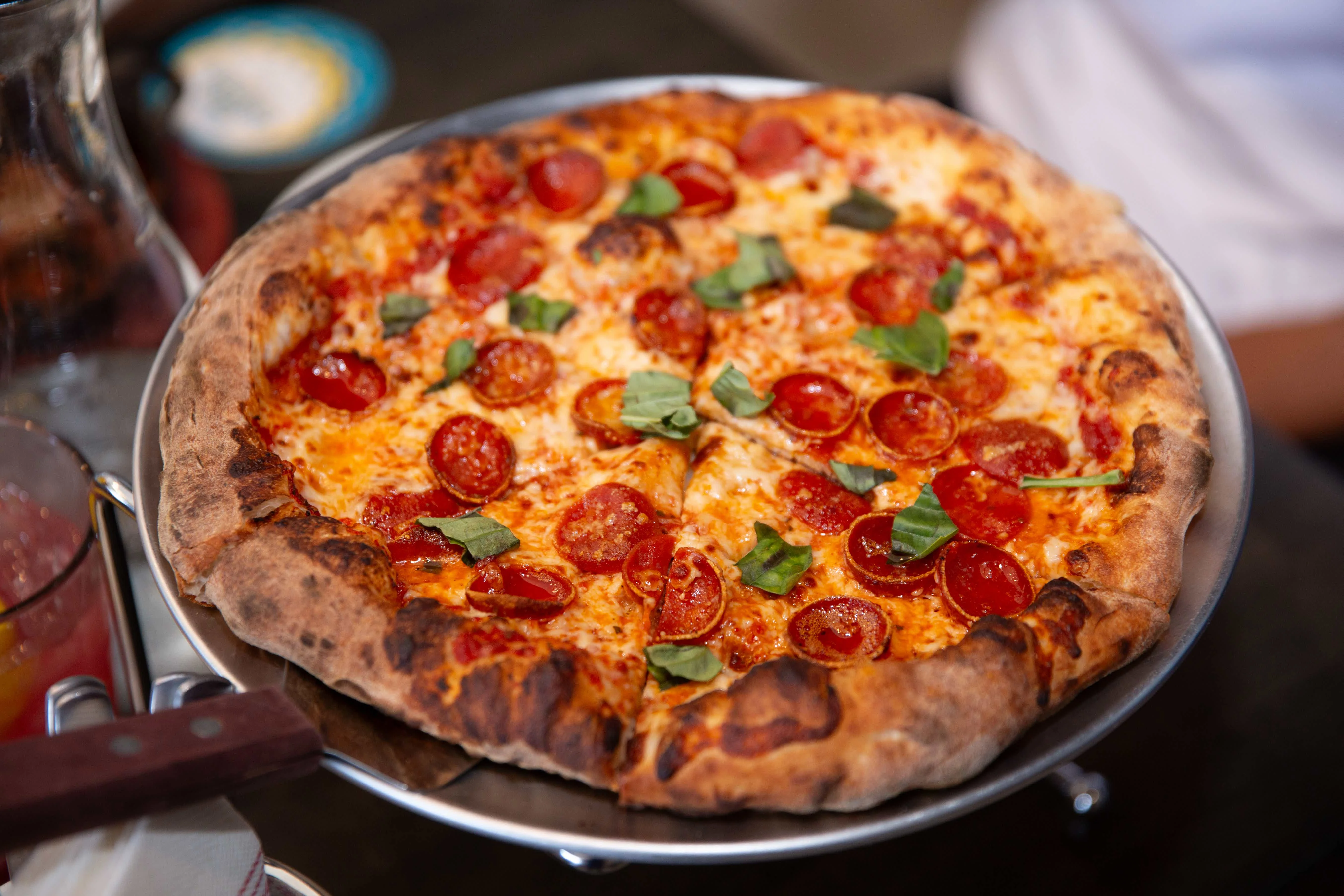 Pepperoni pizza with fresh basil on a metal serving tray