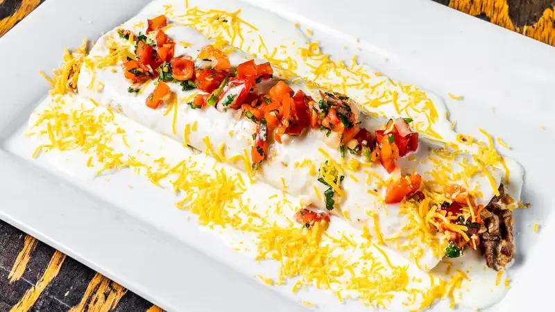 A delicious enchilada topped with cheese, tomatoes, and sour cream.