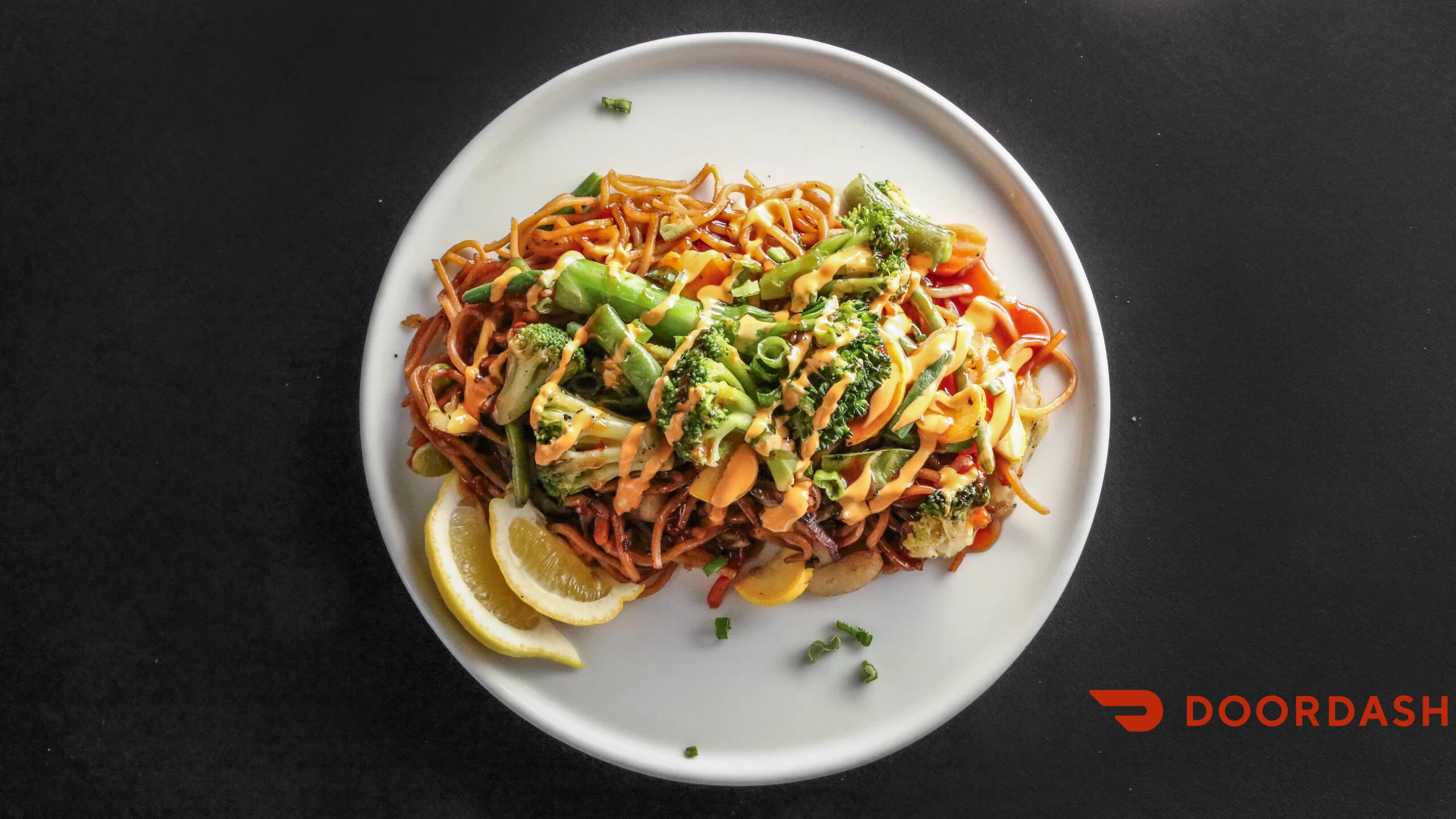 A serving of stir-fried noodles topped with green vegetables and a creamy sauce, garnished with lemon slices.