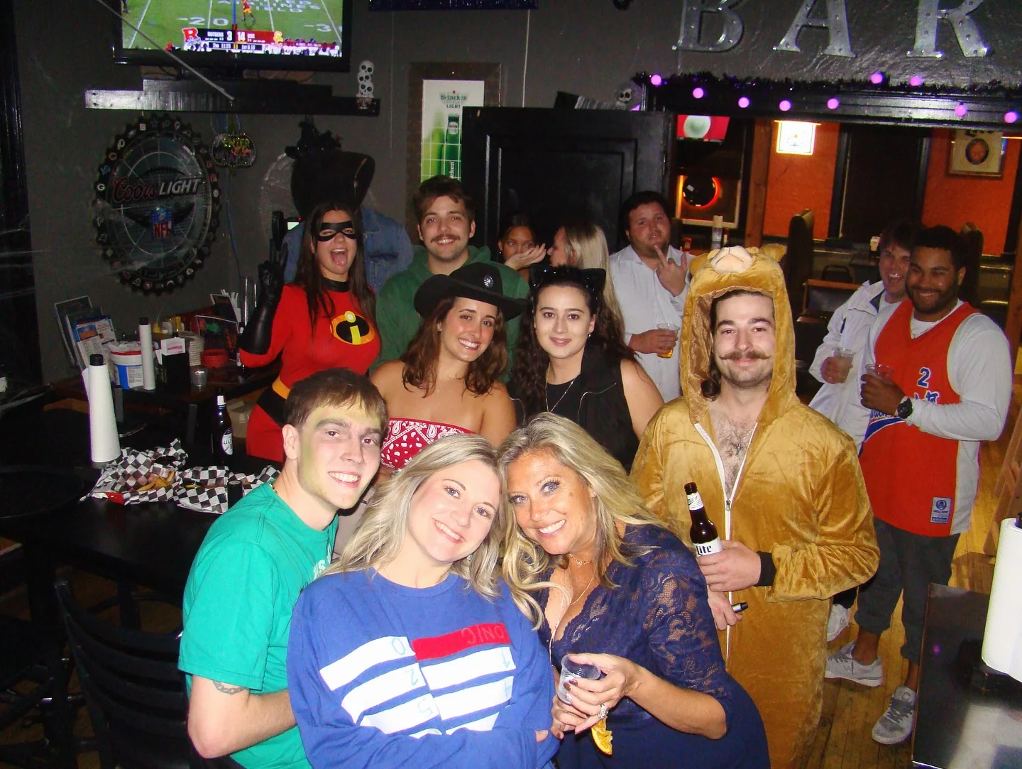 Group in Halloween costumes posing inside a lively sports bar