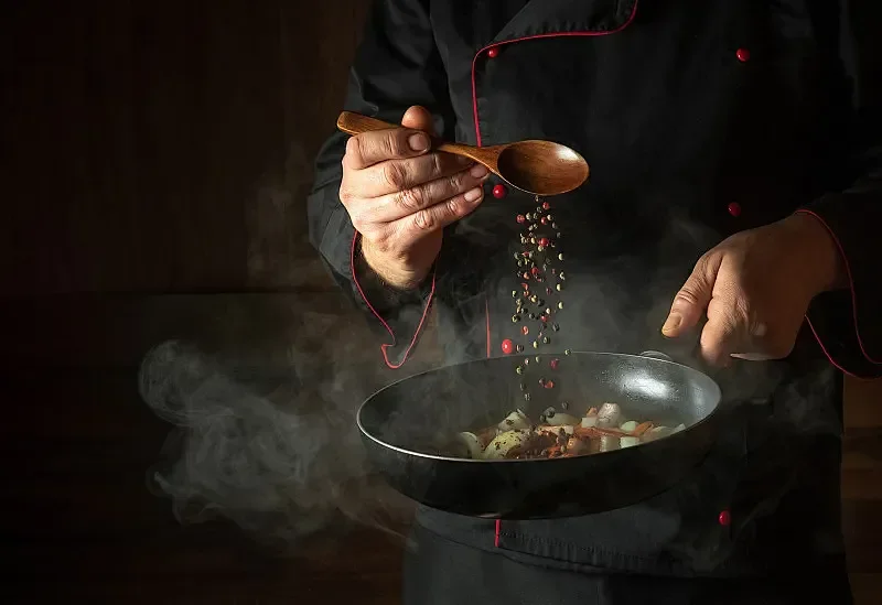 Chef seasoning a pan of sizzling stir-fry
