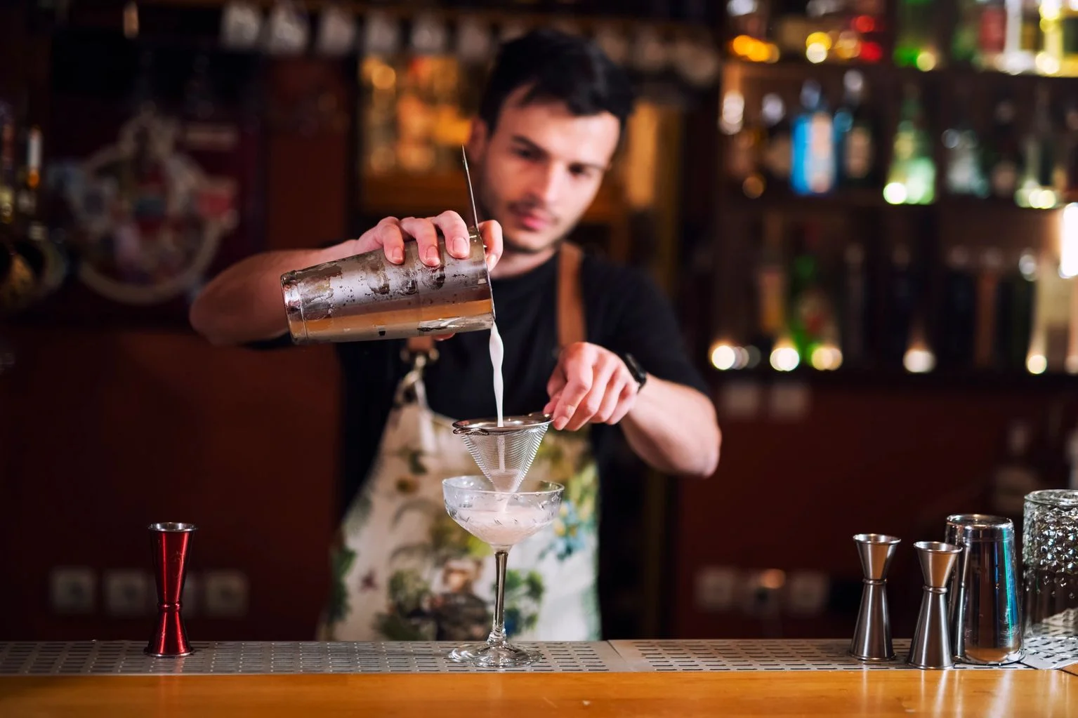 Bartender pouring a cocktail through a strainer at a stylish bar