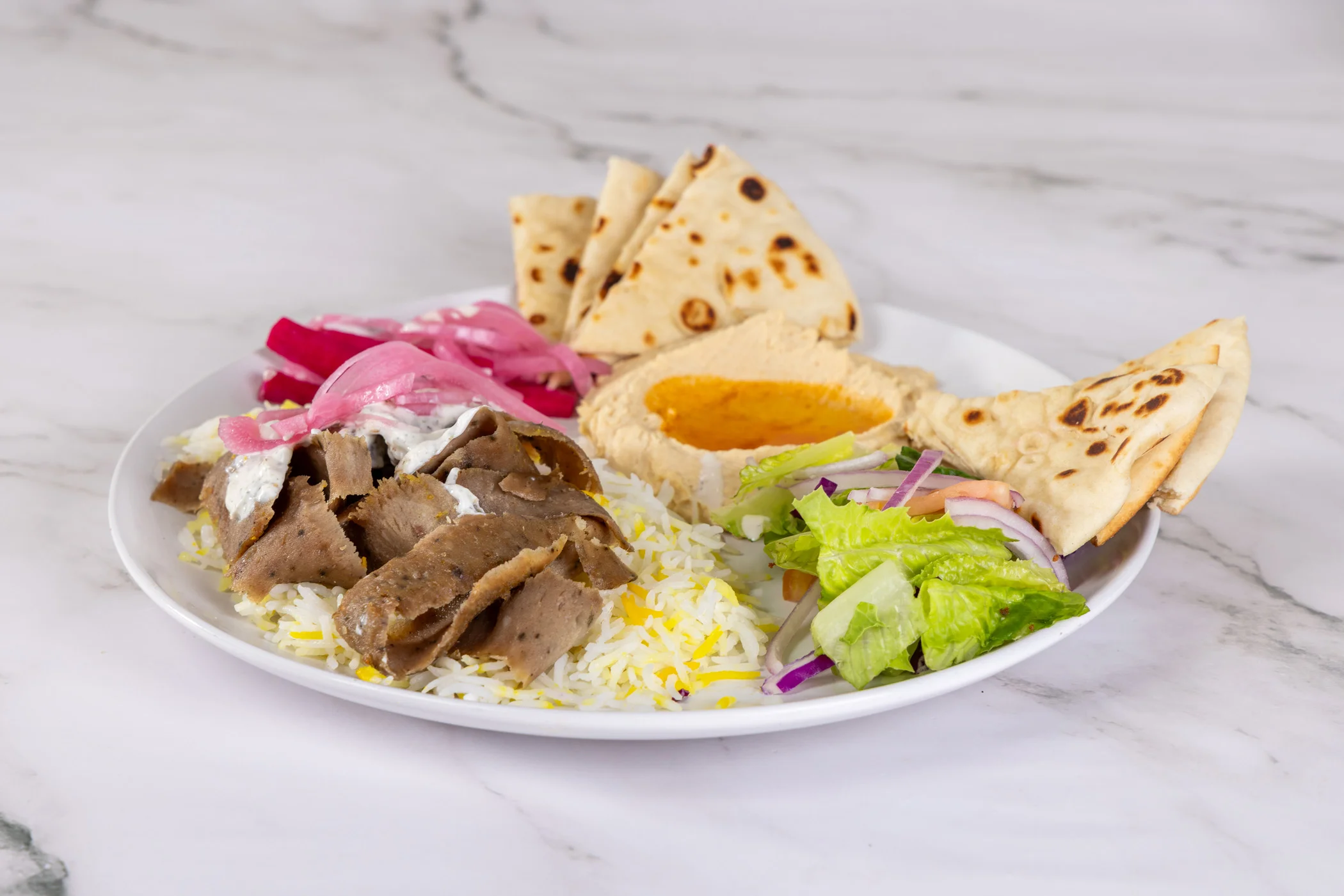 A delicious gyro plate with meat, vegetables, and sauce served on a platter.