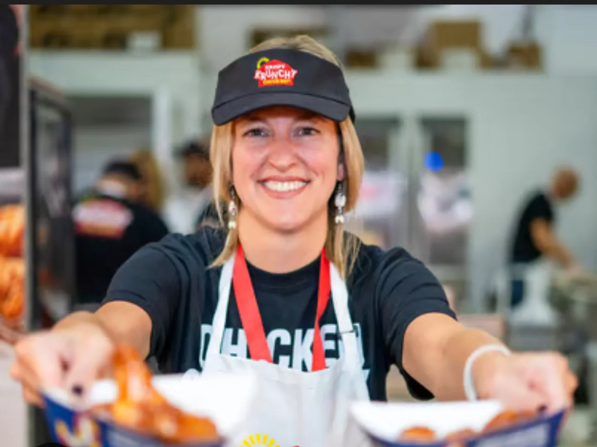 Smiling server presenting crispy chicken wings at a vibrant food stall