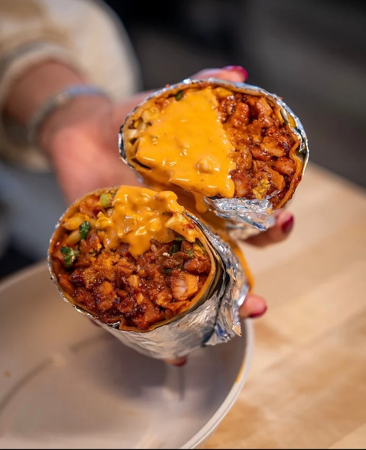 A close-up of two burritos being held, with melted cheese and a mix of ingredients visible inside.