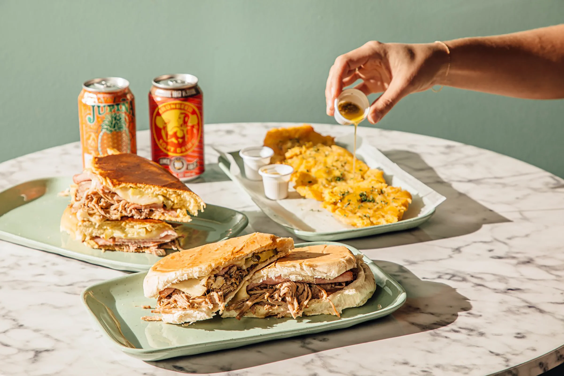 Cuban sandwich with tostones and drinks on a marble table