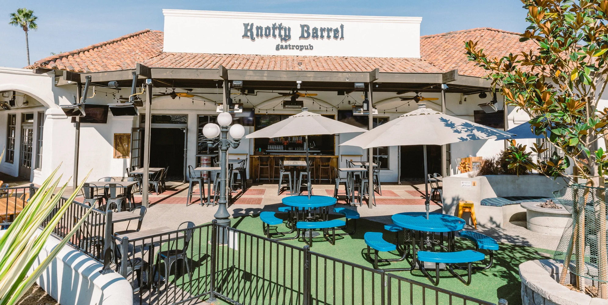 The exterior of a gastropub featuring outdoor seating, umbrellas, and a welcoming sign.