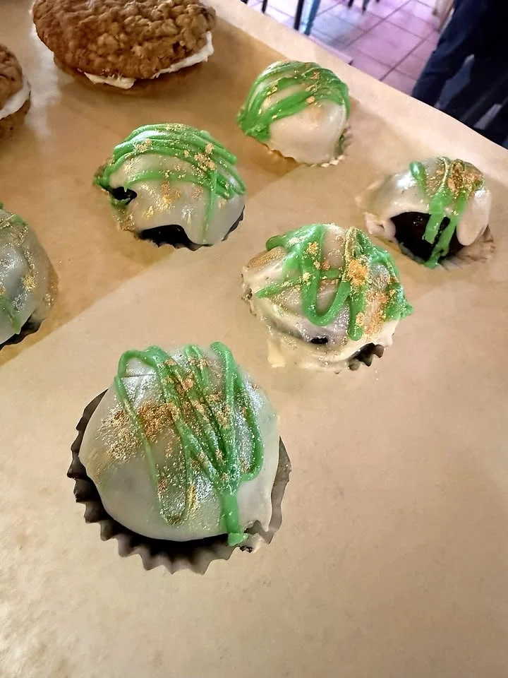 A variety of decorated dessert balls with green icing and gold accents, displayed on a parchment-lined surface.