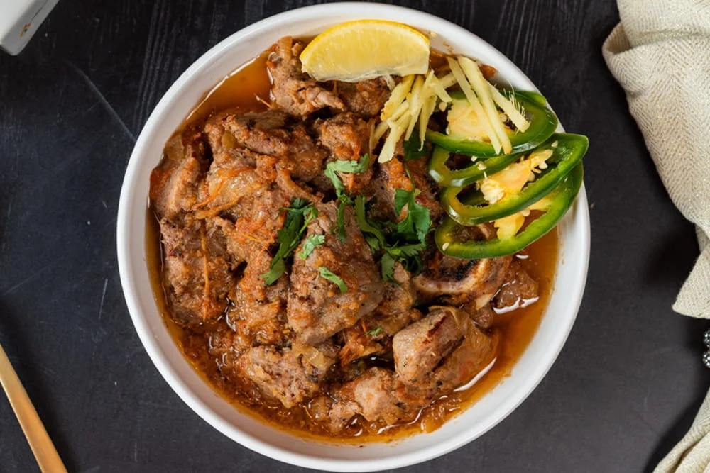 A delicious serving of Goat Korma in a bowl, garnished with herbs.