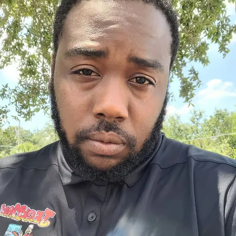 Close-up of a man with a beard wearing a black shirt outdoors.