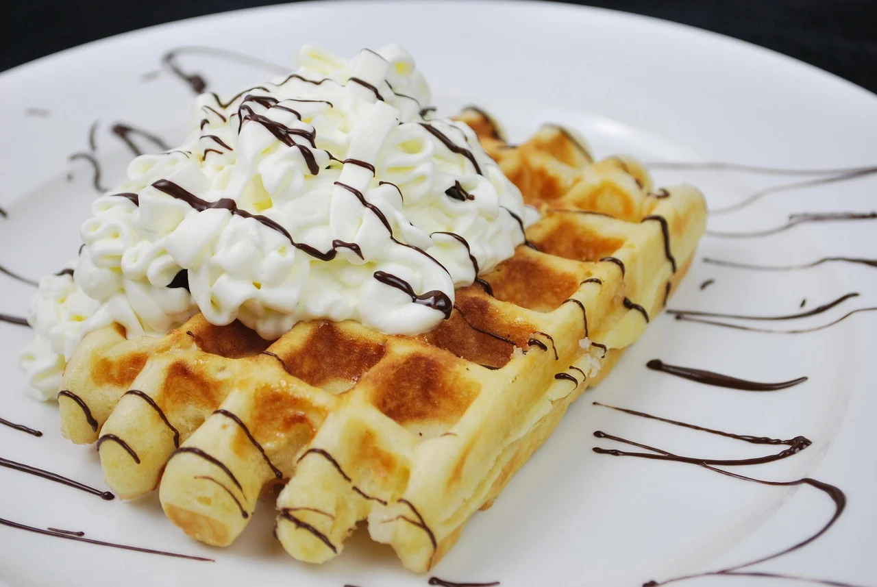 Belgian waffle topped with whipped cream and chocolate drizzle
