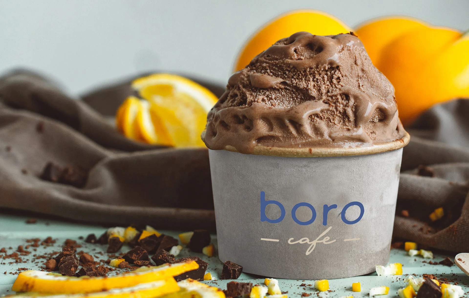 A cup of chocolate ice cream topped with a rich, creamy texture, surrounded by chocolate pieces and fresh orange slices.