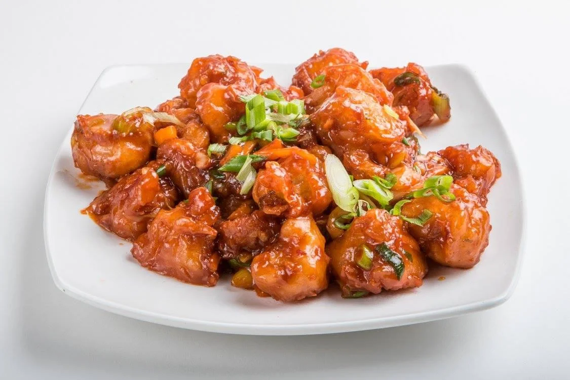 Sweet and tangy battered fried cauliflower pieces garnished with chopped green onions, served on a white plate.