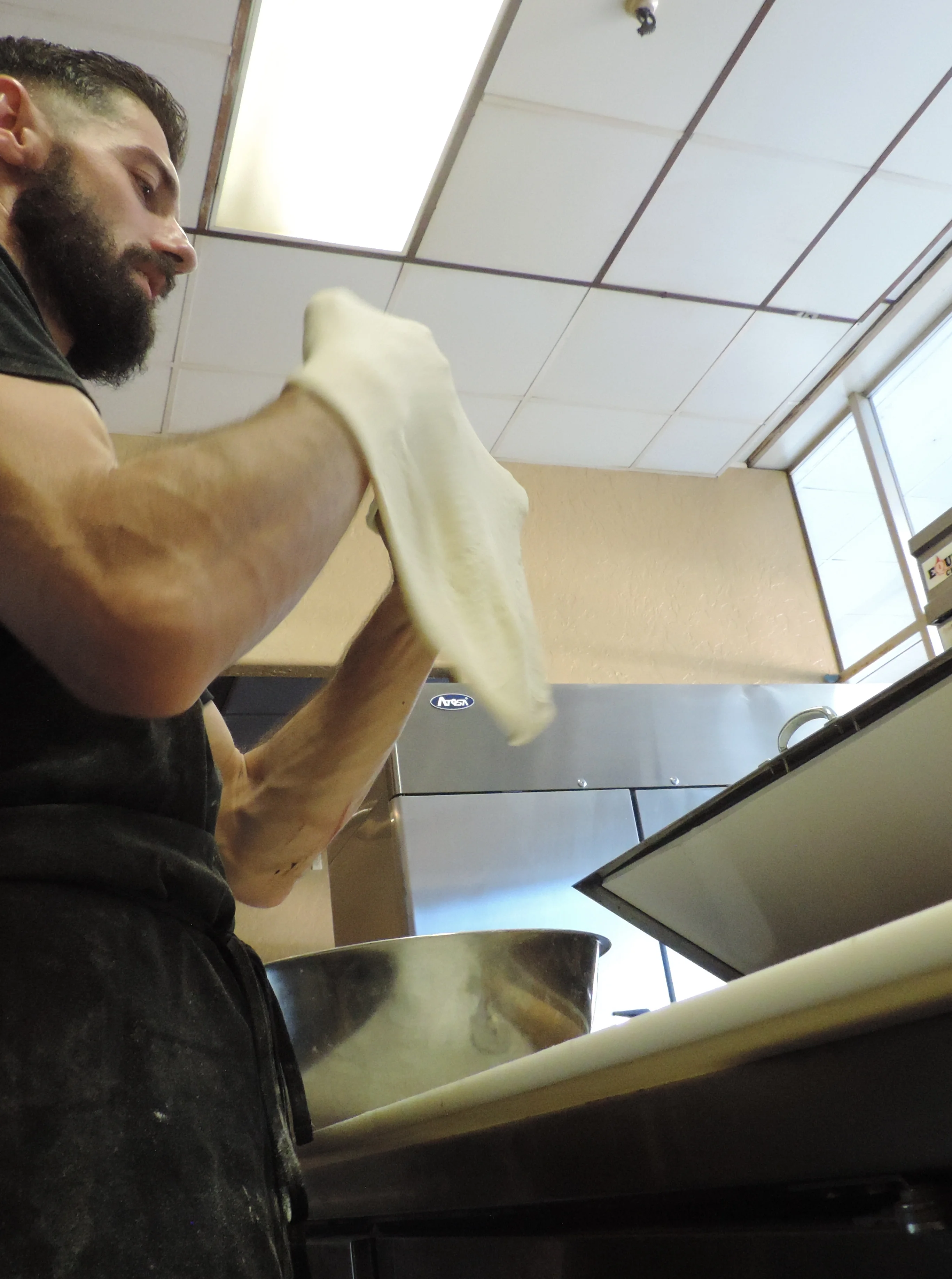 A hand wearing a glove is sprinkling a substance into a stainless steel bowl in a kitchen environment.