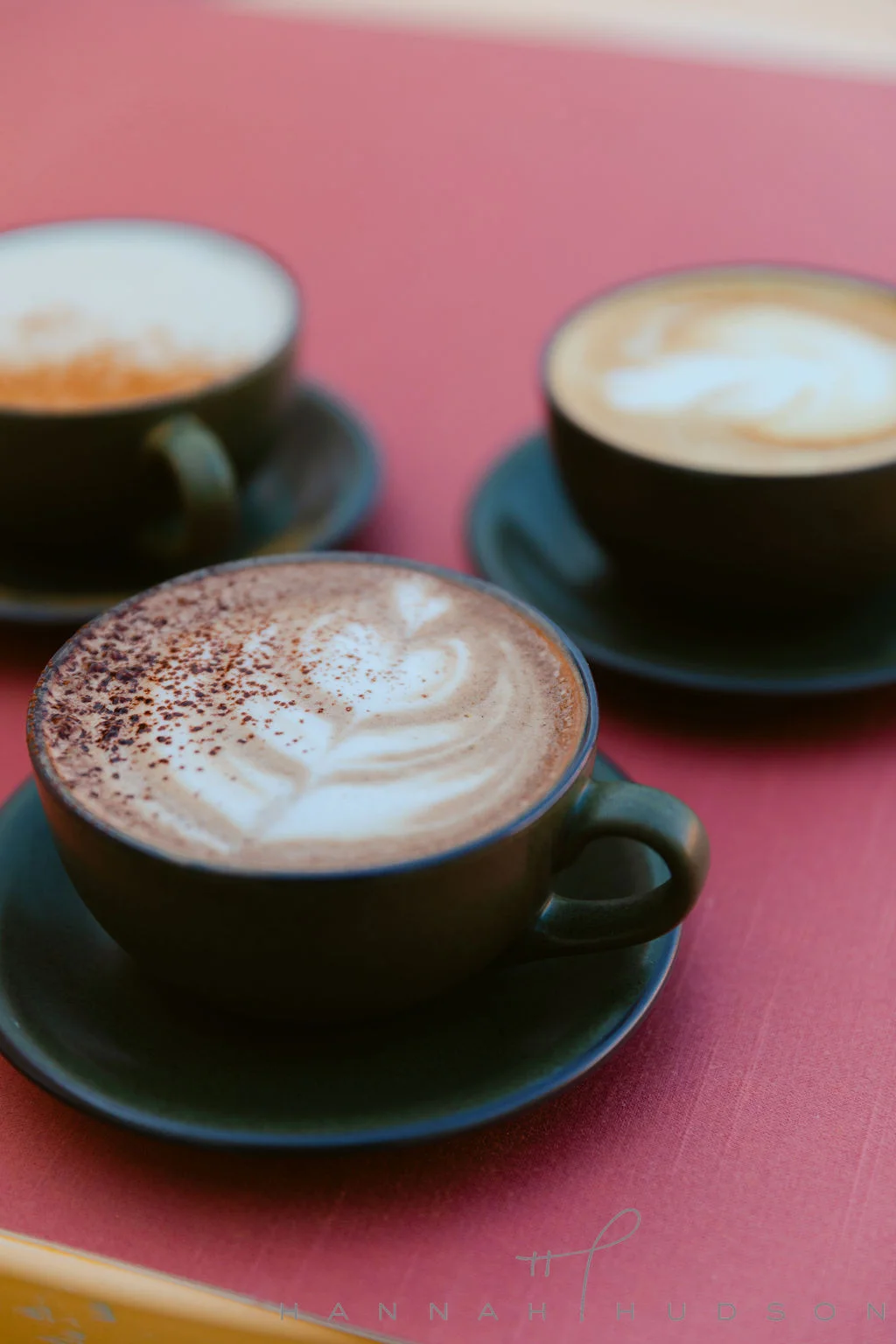 Three cappuccino cups with latte art on a pink café table