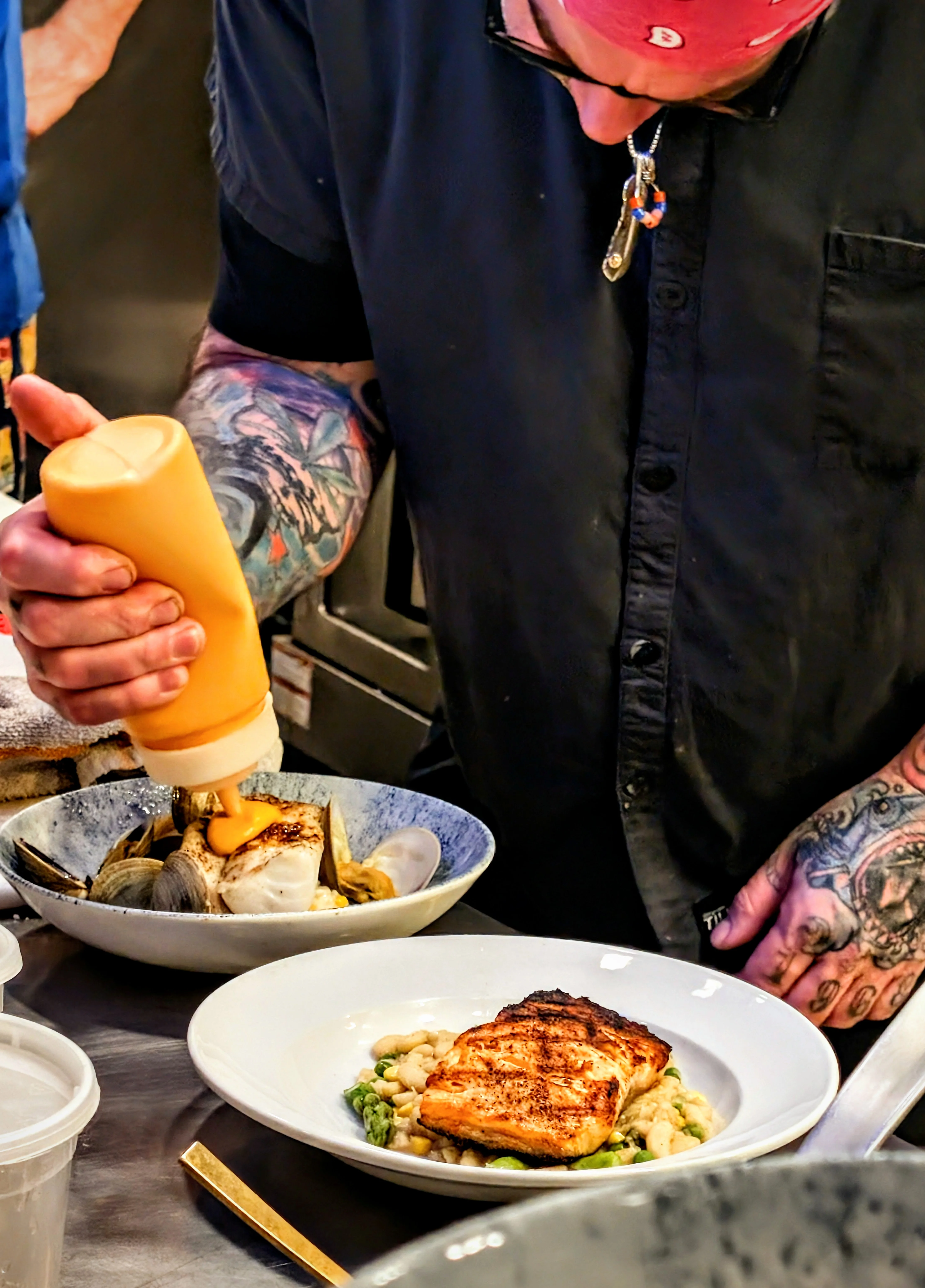 A chef is preparing a plate of food, drizzling sauce over a well-cooked salmon and vegetables.