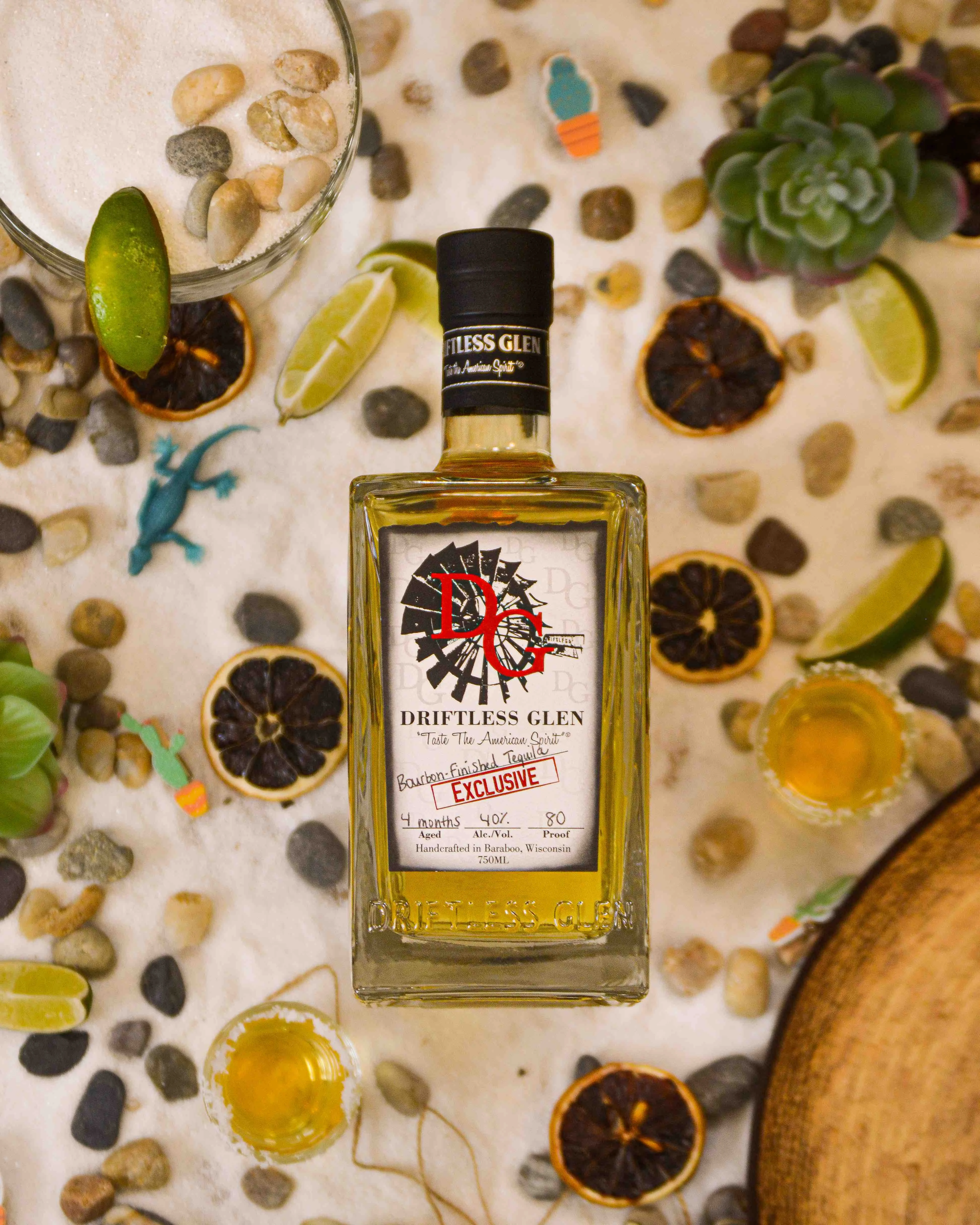 Bourbon-Finished Tequila sits by some limes and dried orange slices in the sand