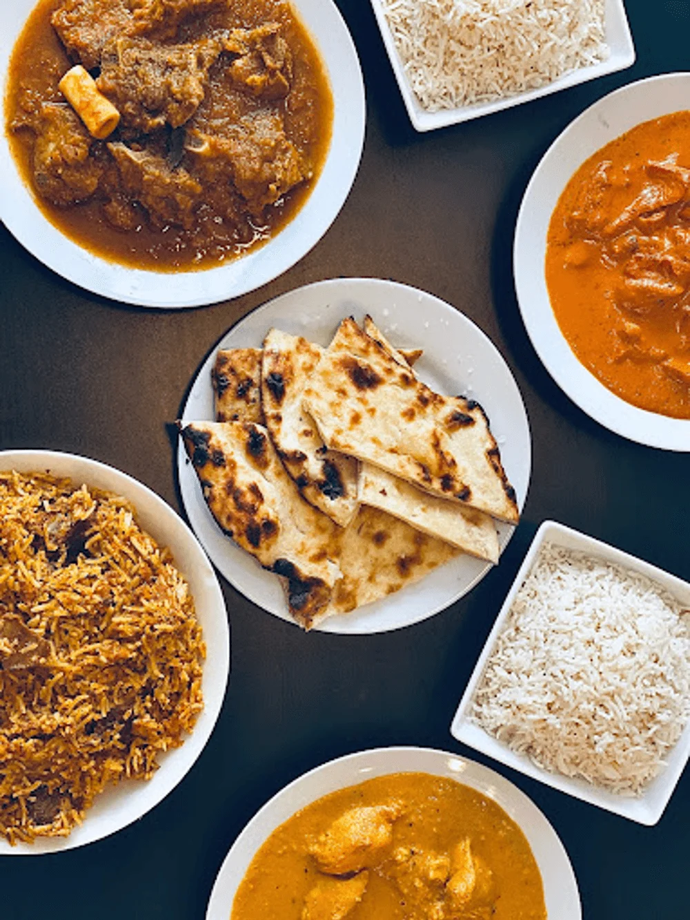 Indian meal with white rice, a bowl of brown curry, salad, and naan bread.