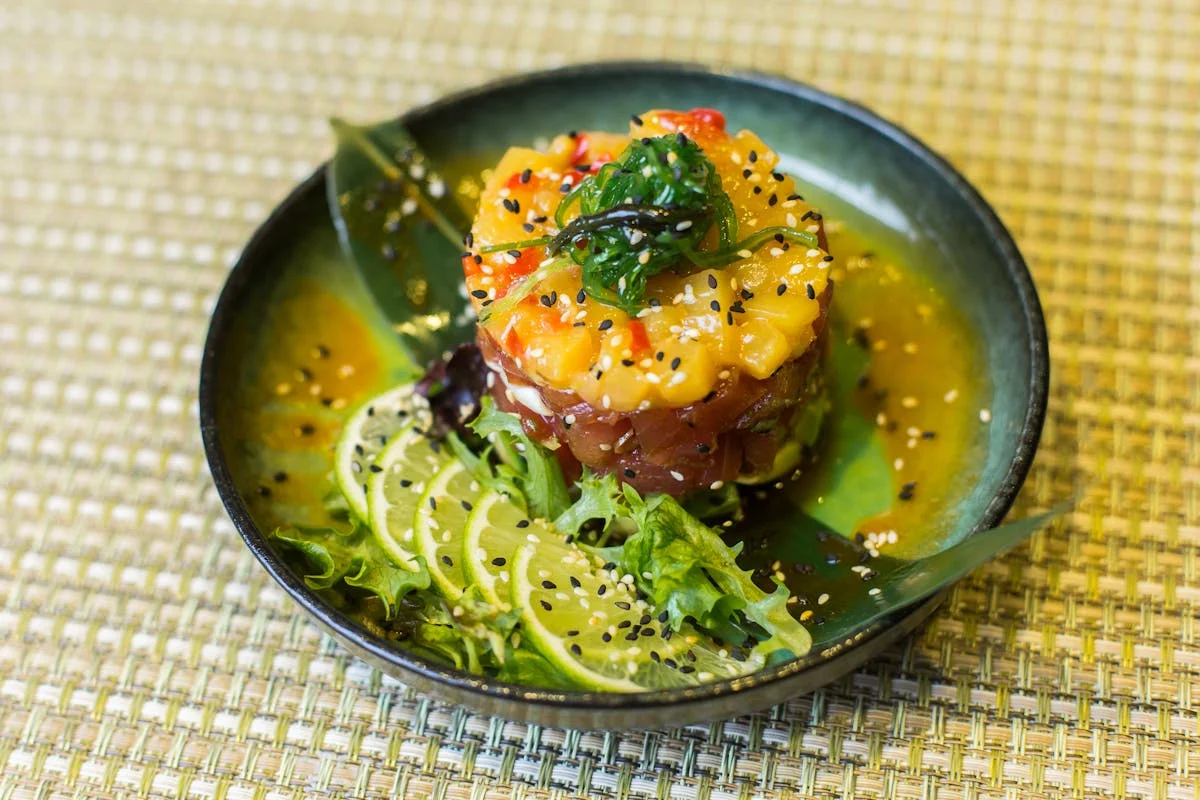 A colorful dish featuring tuna and mango with lime slices and sesame seeds.