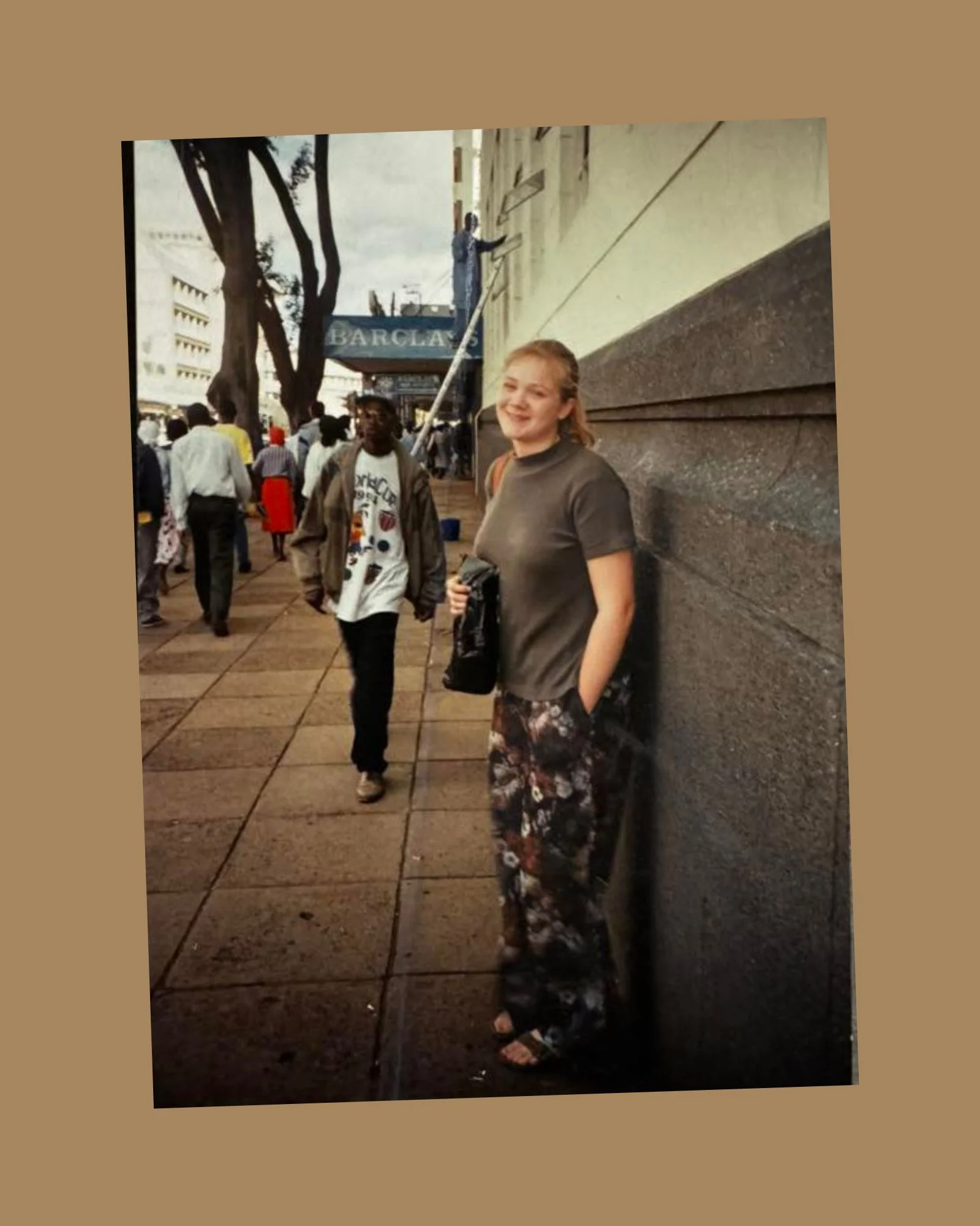 A woman standing on a city sidewalk with a camera, surrounded by pedestrians.