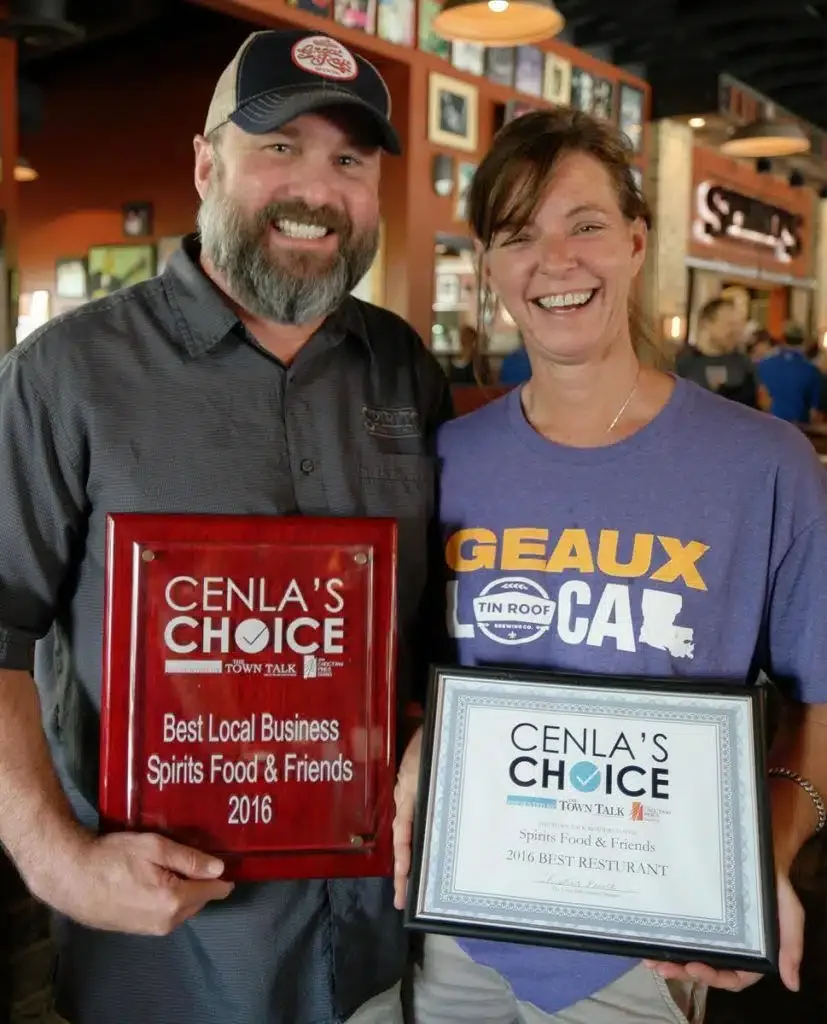 Two restaurant owners proudly holding awards for best local business and restaurant